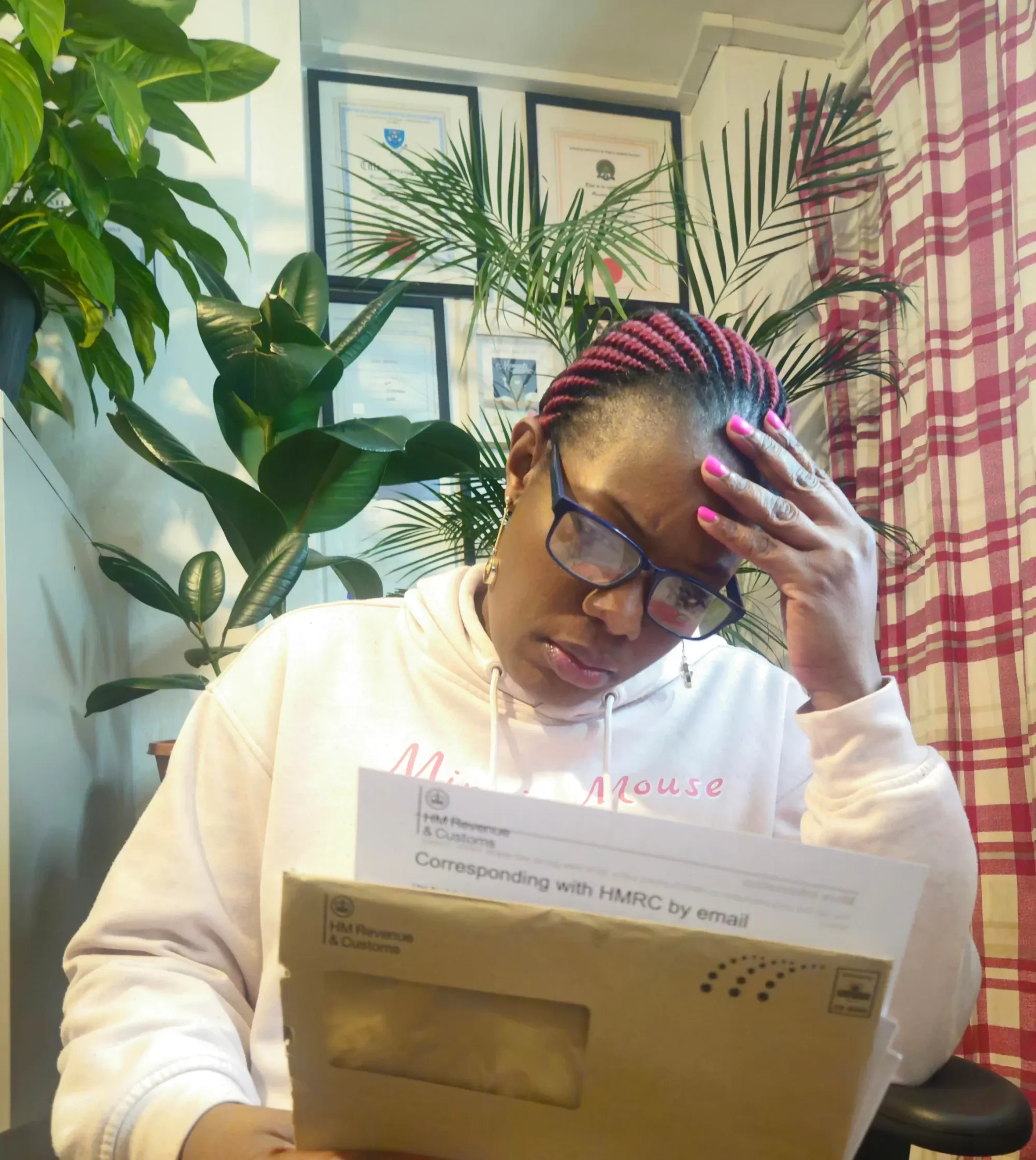 A woman wearing glasses and a hoodie sits at a desk holding an HMRC envelope, looking stressed — highlighting the anxiety of receiving an audit letter.